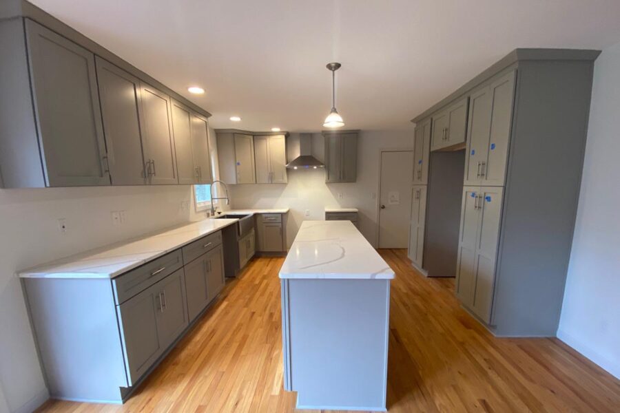 Kitchen after remodeling, with gray cabinets, white countertops, a central island and wood flooring