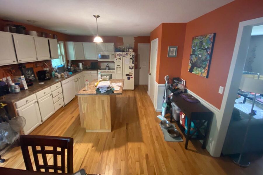 Kitchen before remodeling, with white cabinets, a wooden island, hardwood flooring and orange walls