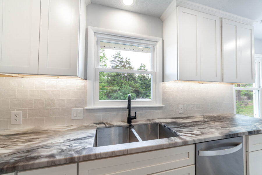 Kitchen with white cabinets, veined gray and white countertops, white tile backsplash, stainless steel sink and black faucet