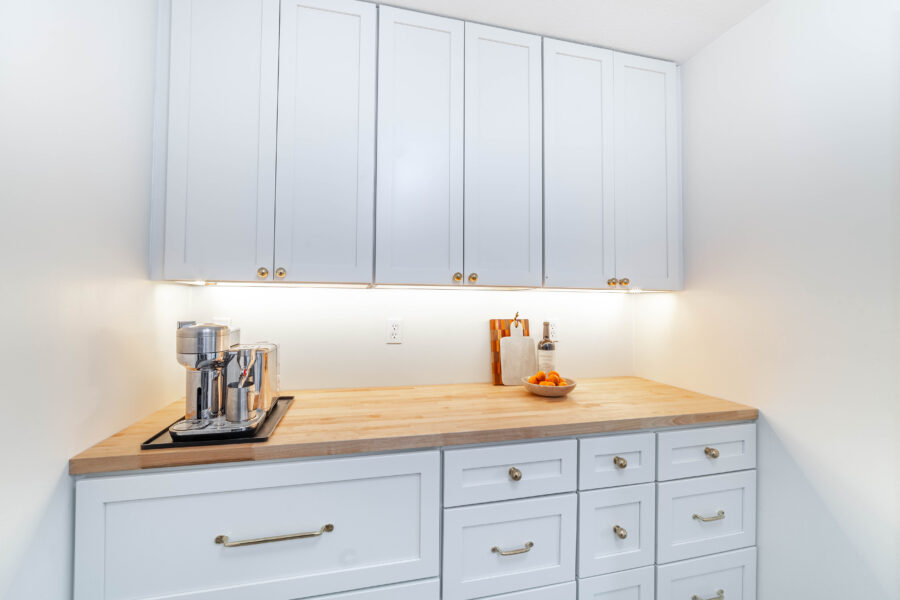 Built-in cabinet and counter area with light cabinets, a wood countertop, under-cabinet lighting, and brass pulls
