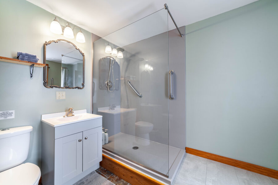 Bathroom with a toilet, sink vanity, ornate mirror, wall lights, towel shelf and glass-enclosed shower