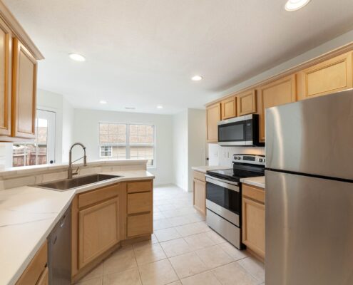 Kitchen with wood cabinets, white counters, a sink, stainless steel appliances, tile flooring and a window