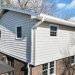 House exterior with light gray horizontal siding, white-framed windows, white gutters and a red brick lower wall