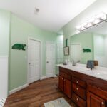 Bathroom with pale green walls, a wooden double-sink vanity, a large mirror and a glass shower enclosure