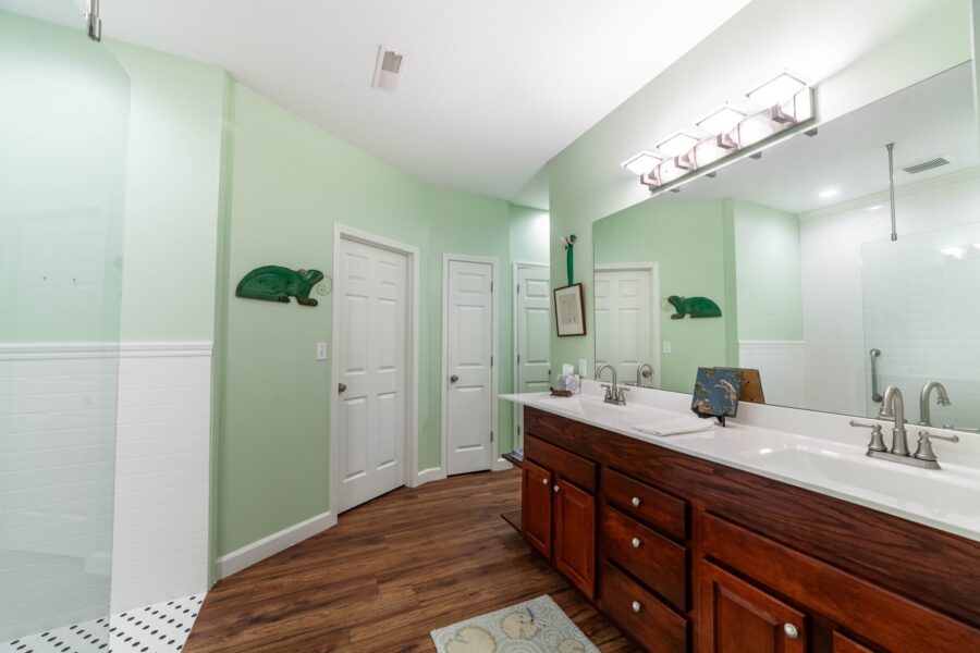 Bathroom with pale green walls, a wooden double-sink vanity, a large mirror and a glass shower enclosure
