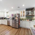 Kitchen with white cabinets, a stainless steel refrigerator and dishwasher, wood flooring and a glass dining table
