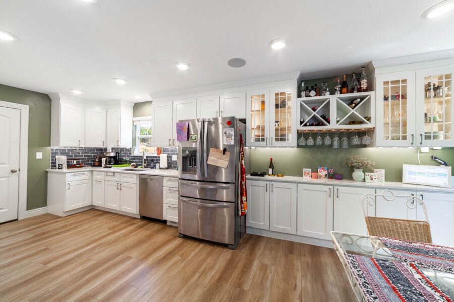 Kitchen with white cabinets, a stainless steel refrigerator and dishwasher, wood flooring and a glass dining table